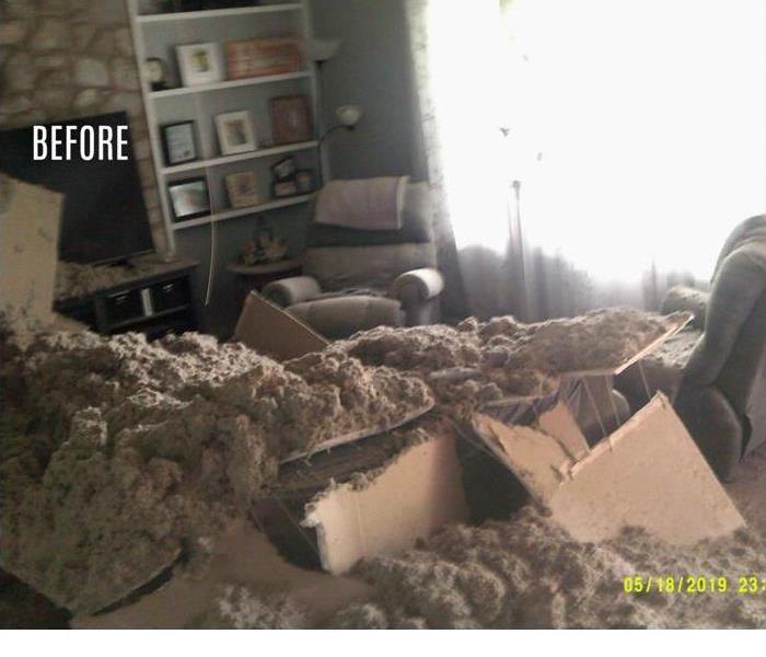 Living room with collapsed ceiling with floor and furniture covred in blown insulation debris